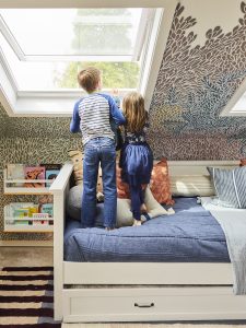 Two children standing on a bed looking out of a skylight